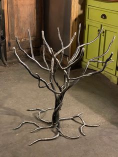 a metal tree sculpture sitting on top of a cement floor next to a green cabinet