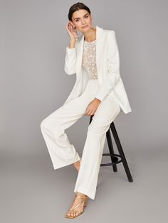 a woman sitting on top of a chair wearing white pants and a blazer jacket