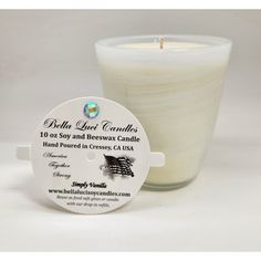 a white candle sitting next to a glass container with a label on the front that says, beth leer candles 10 soy and beeswax candle hand poured in cross ca usa