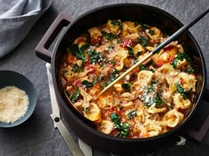 a pot filled with pasta and spinach next to a bowl of grated parmesan cheese