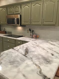 a kitchen with green cabinets and white marble counter tops, along with stainless steel appliances