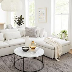 a living room with white couches and pillows on top of the sofa, next to a round coffee table