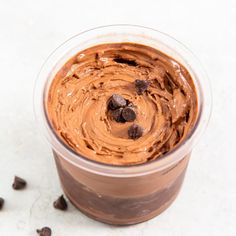 a plastic cup filled with chocolate pudding on top of a white table next to some chocolate chips