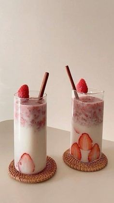 two glasses filled with yogurt and strawberries next to each other on a table