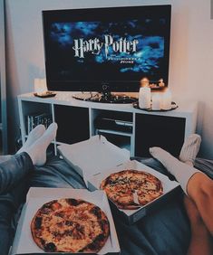 two pizzas sitting in front of a tv with harry potter logo on the screen