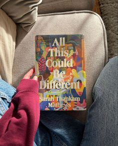 a person sitting on a couch holding a book in their hand and reading it to the camera