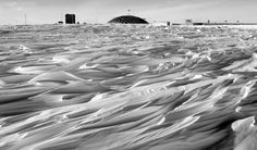 black and white photograph of sand dunes with buildings in the background