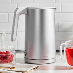 an electric kettle sitting on top of a counter next to cups and bowls filled with raspberries