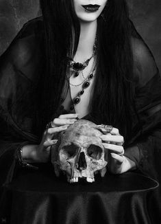 a woman with long hair holding a skull in front of her face and wearing black makeup