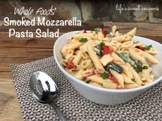 a white bowl filled with pasta sitting on top of a table next to a spoon