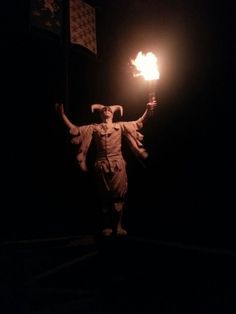 a man holding a lit candle in the dark with his arms outstretched and hands out