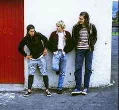 three young men standing next to each other in front of a red and white wall