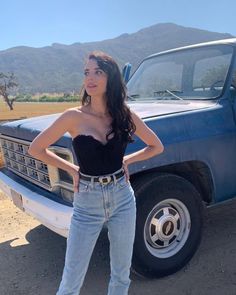 a woman standing in front of a blue pickup truck with her hands on her hips