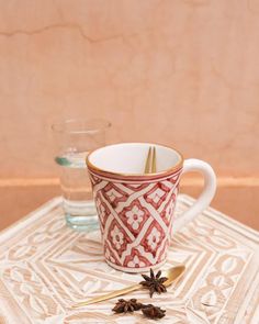 a red and white coffee cup sitting on top of a table next to two glasses