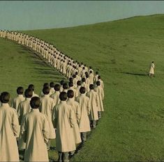 a large group of people walking across a lush green field next to a man in a white suit