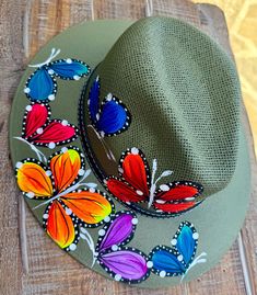 a green hat with colorful butterflies on it sitting on a wooden table next to another hat