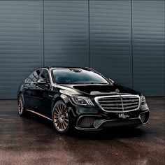 a black mercedes s - class parked in front of a garage door with gold rims