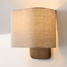 a lamp mounted on the side of a wall with a beige shade covering it's face