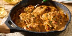 a skillet filled with meat and sauce on top of a table next to wine glasses