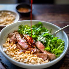 a bowl filled with meat and vegetables on top of a wooden table