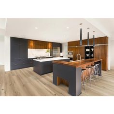 a modern kitchen with wooden floors and gray cabinets is pictured in this image, there are three bar stools at the center of the island