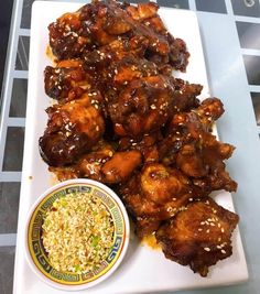 chicken wings with sesame seeds and dipping sauce on a white platter next to a bowl of rice