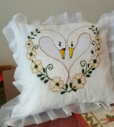 a white pillow with two swans in the shape of hearts and flowers on top of it