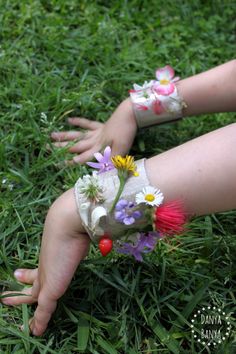 a child's hand reaching for flowers in the grass with their hands on it