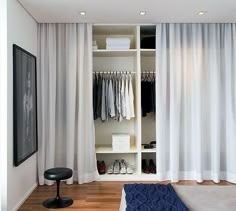 an open closet with clothes and shoes on the floor, next to a white wall