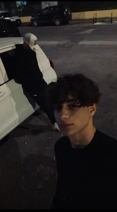 a young man standing next to a white car