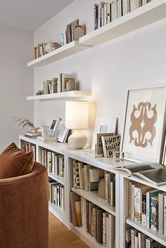 a living room filled with lots of books on top of a white book shelf next to a brown chair