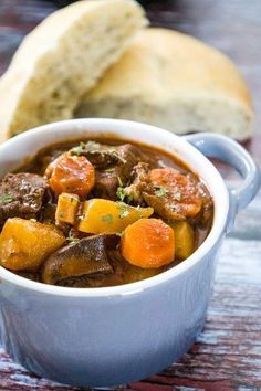 a close up of a bowl of stew with bread in the background