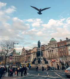 a large bird flying over a busy city street with people walking on the side walk