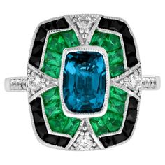 A striking and intriguing jewel, indeed. This bold and colorful Art Deco style ring highlights a gorgeous gleaming emerald cut London blue topaz framed in eye-catching contrast by French cut emerald and black onyx. Each side and shoulders set off with round diamond with milgrain edge. Ring Information Style: Edwardian Metal: 18K White Gold Weight: 6.50 g. (approx. total weight) Ring Size: US3-8 Center Gemstone Type: London Blue Topaz Shape: Octagon Size: 8 x 5.5 mm. Number: 1 Weight: 2.00 Carat Luxury Blue Art Deco Rings, Vintage Emerald Rings Blue Nile, Luxury Enamel Art Deco Rings, Gem Rings Stones 1stdibs, Edwardian Onyx Rings, Luxury Emerald Gemstones With Accent Stones, Luxury Multi-stone Emerald Cut Emerald Ring, Luxury Sapphire Ring With Emerald Cut And Gemstone Accents, Luxury Emerald-cut Sapphire Ring With Gemstone Accents