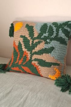 a crocheted pillow with tassels on top of it sitting on a bed