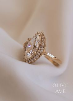 an engagement ring with a pear shaped diamond surrounded by smaller round diamonds on a white cloth