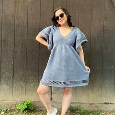 a woman standing in front of a wooden wall wearing a blue dress and white tennis shoes