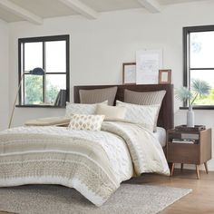 a bed with white and beige comforters in a bedroom next to two windows,