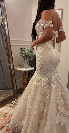 a woman in a wedding dress looking at herself in the mirror with her back to the camera