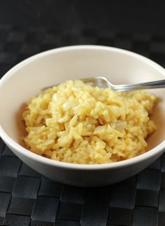 a white bowl filled with rice sitting on top of a black table next to a spoon