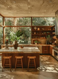 a kitchen with wooden cabinets and marble counter tops, surrounded by large windows that look out onto the forest