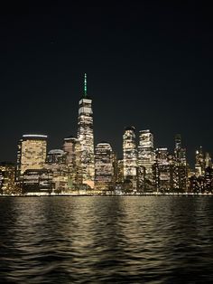 the city skyline is lit up at night as seen from across the water in new york