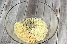 a glass bowl filled with shredded cheese on top of a wooden table