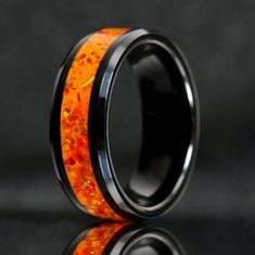 an orange and black wedding ring with gold flakes inlaying the center, on a reflective surface