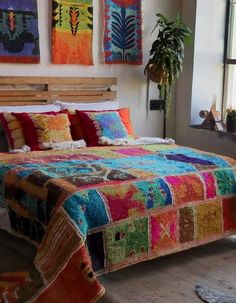 a bed with colorful bedspread and pillows in a room filled with potted plants