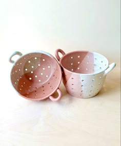 two pink and white ceramic dishes sitting on top of a wooden table next to each other