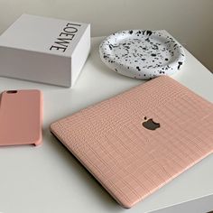 an apple laptop sitting on top of a white table next to a pink iphone case