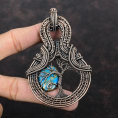 a hand holding a silver pendant with a blue stone in the center and intricate designs on it