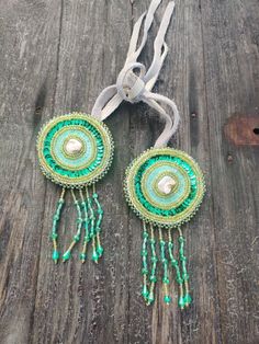 two green and white beaded earrings hanging from a wooden table next to a piece of string