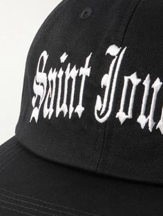 The LA streetwear scene is obsessed with Old English lettering – it's been blasted across baseball caps since the early '90s. Tapping co-founder Cali Thornhill Dewitt's SoCal roots, SAINT Mxxxxxx's trucker hat is made from cotton-twill and embroidered with 'Saint Journey' in the script. Classic Hats With Logo Print For Streetwear, Casual Baseball Cap With Graphic Print And Flat Brim, Graphic Print Snapback Hat With Curved Bill For Streetwear, Urban Letter Print Hat For Baseball Season, Urban Hats For Baseball Season Streetwear, Urban Hats For Streetwear During Baseball Season, Urban Streetwear Hats For Baseball Season, Curved Bill Hats With Logo Print For Streetwear, Logo Snapback Hat With Curved Bill For Streetwear